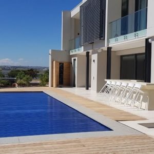 designer pool covers A modern house with a swimming pool and deck featuring pool covers for added safety.