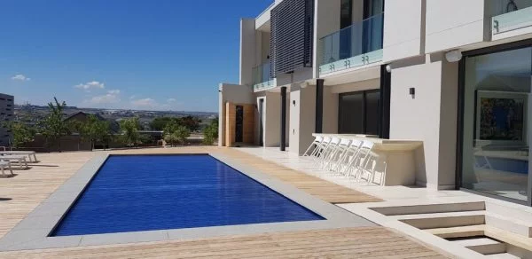 designer pool covers A modern house with a swimming pool and deck featuring pool covers for added safety.