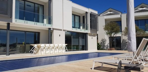 designer pool covers A modern house with a PoolDeck Slatted Automatic Cover 3.5M X 8M and lounge chairs.