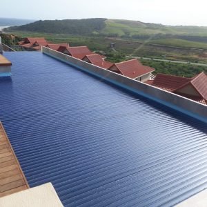 designer pool covers A PoolDeck Slatted Automatic Cover (2500 x 250mm) on a wooden deck with a view of the ocean.