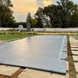 designer pool covers A swimming pool with a Pet & Child Safety Pool Cover (2500 x 250mm) on the ground.