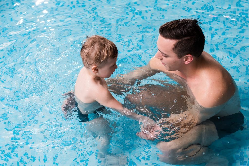 designer pool covers A man and a child playing under a swimming pool cover.