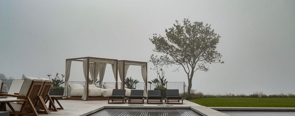 designer pool covers A pool with lounge chairs and a tree in the background, surrounded by pool covers.