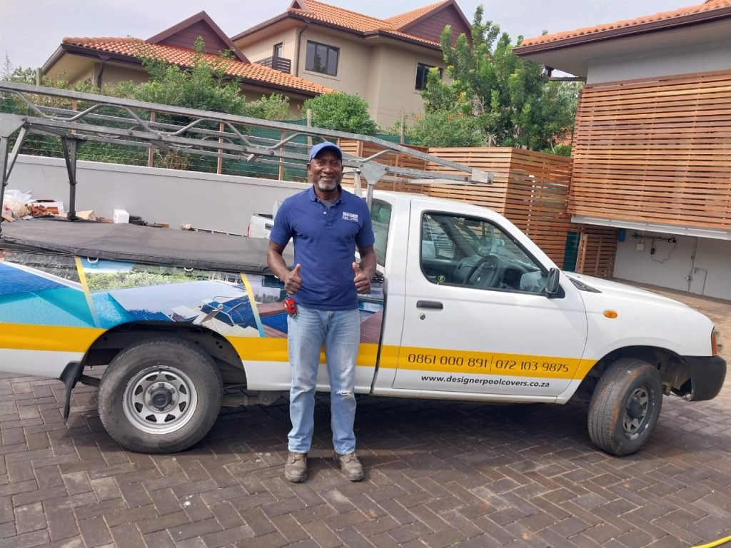 designer pool covers A man standing next to a white truck with a sign on it.