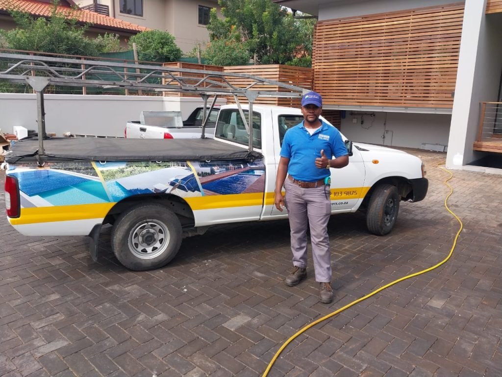 designer pool covers A man standing next to a white truck with a hose.
