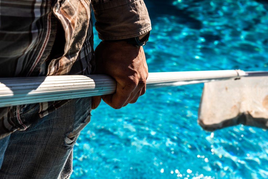 pool pump cleaning designer pool covers A man expertly manages pool water levels while holding a pole in front of a pool.