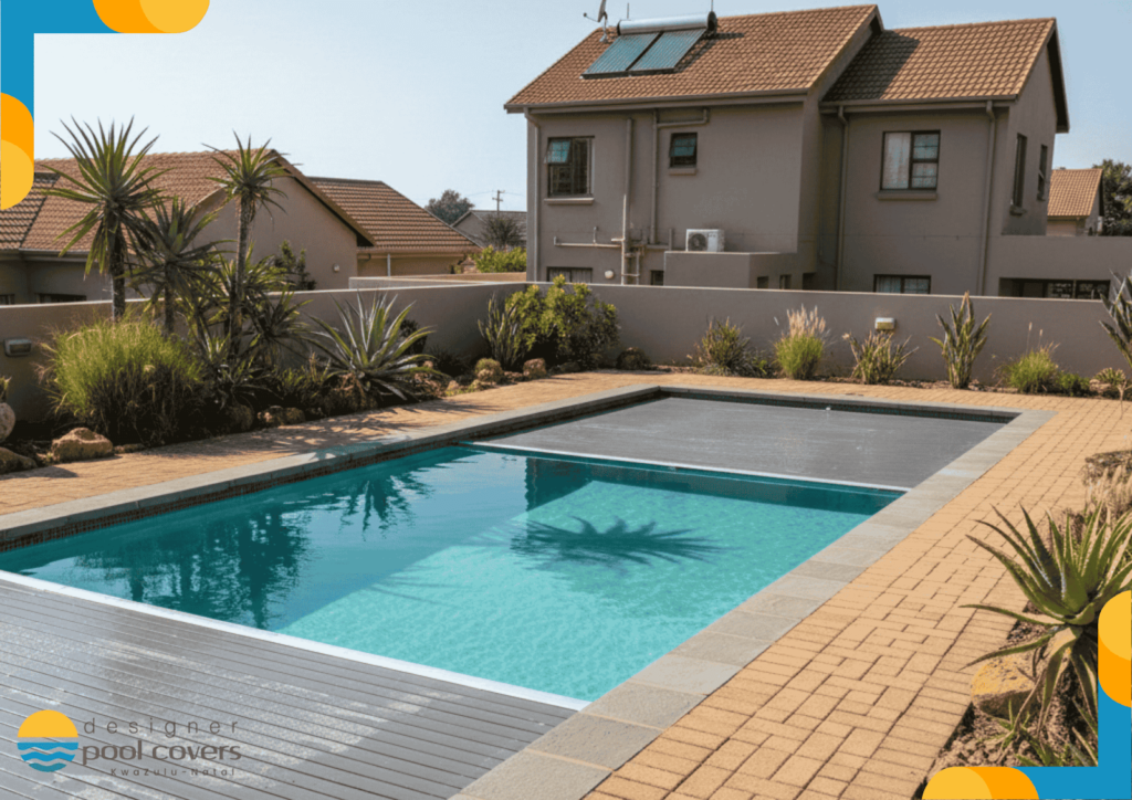 A modern rectangular swimming pool with a partially closed pool cover in a landscaped backyard, adjacent to a house with solar panels on the roof.